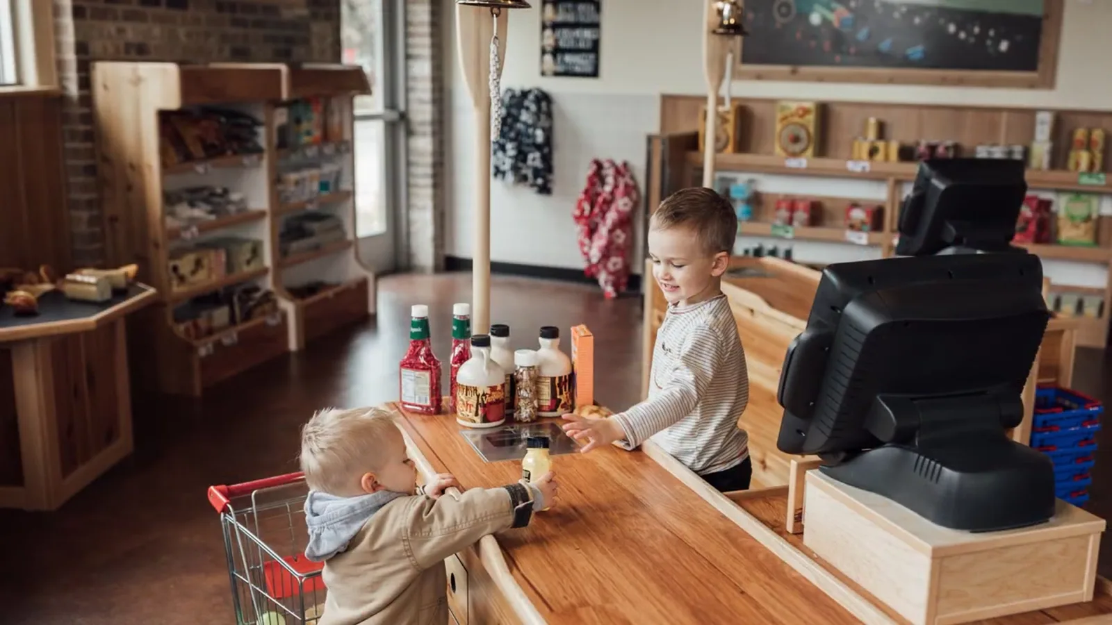 Two children playing shopkeeper in the museum's Trader Joe's pretend grocery store, pushing small carts past shelves of play produce