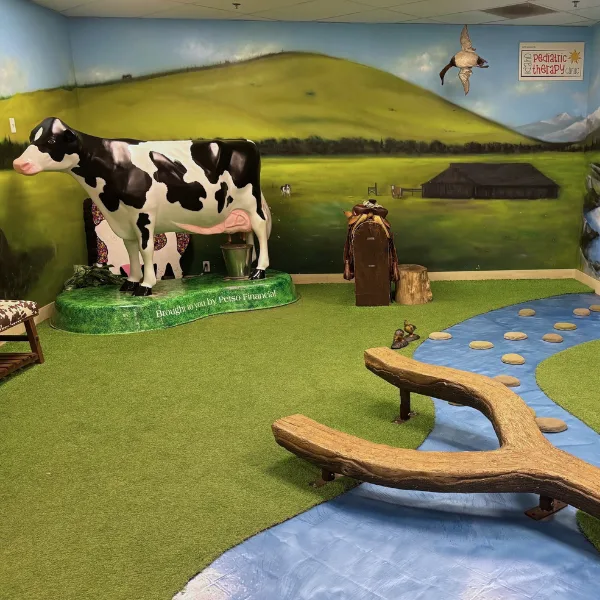 A pretend cow in the corner that kids can milk, beside a pretend river and stones