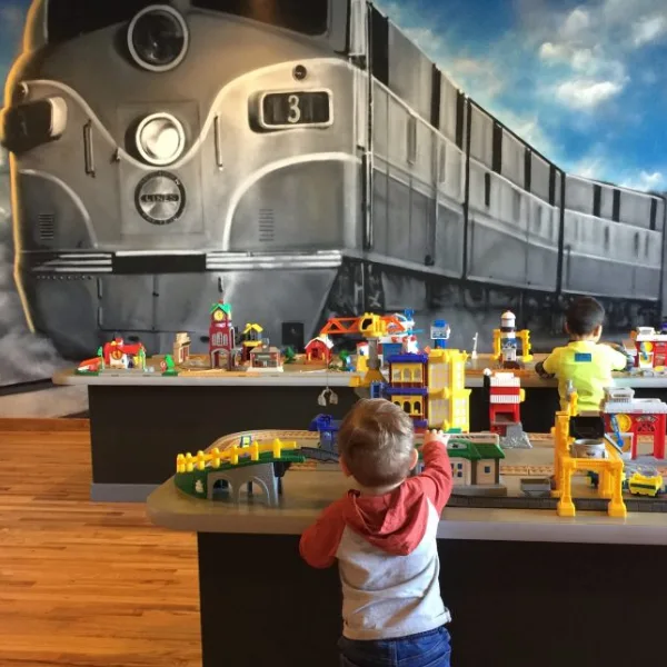Small boy playing at a giant table of trains with a train mural in the background