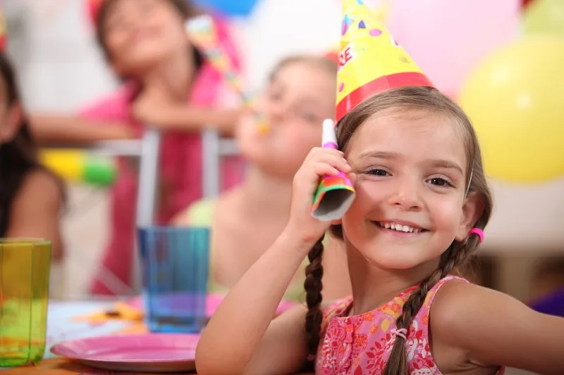 A smiling girl in a birthday party hat celebrating at the museum.