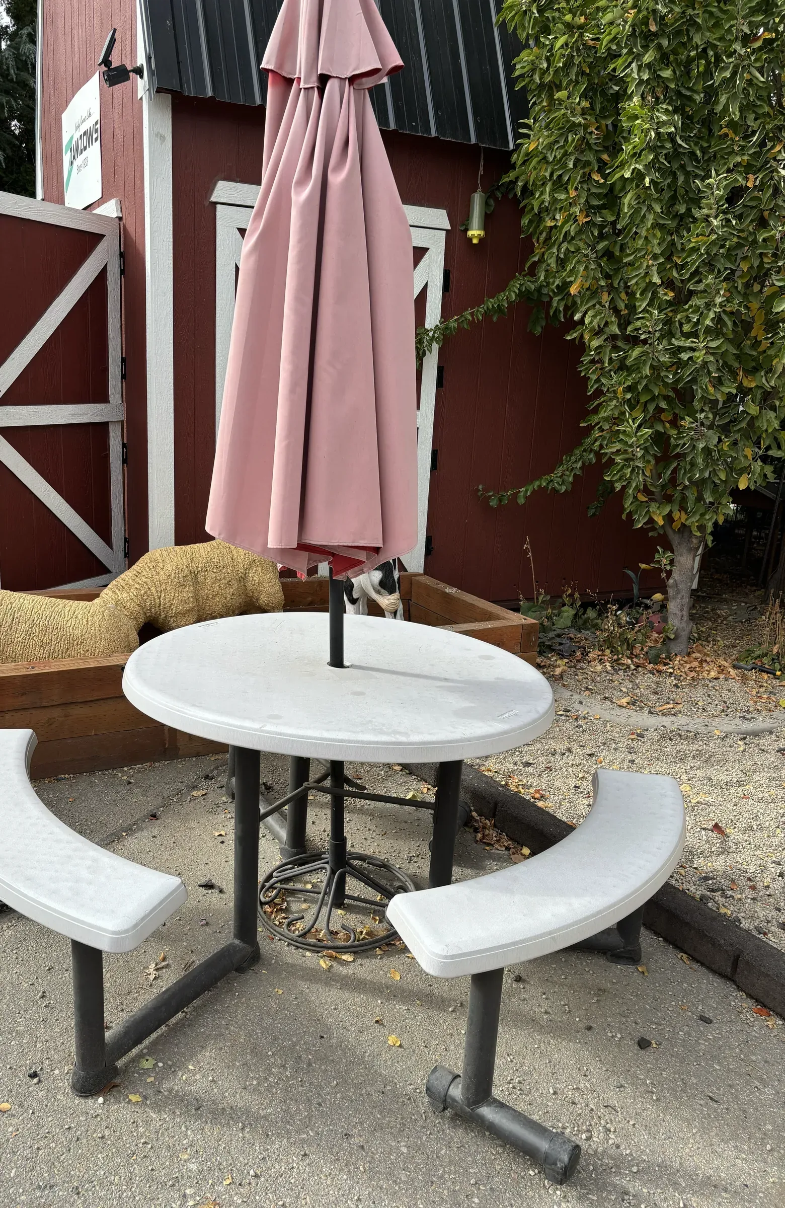 A round table and benches with a folded umbrella beside the red barn in the museum's outdoor area.